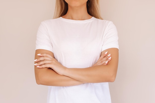 Een bijgesneden opname van een jonge blonde vrouw in een wit T-shirt die haar armen op haar buik kruist