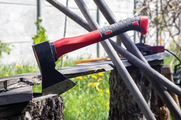 Een bijl met een rood handvat duikt in een boomstronk Zagerij operatie concept houtbewerking Stomp en bijl bij zonnig weer Brandhout voorbereiden op de winter Selectieve focus wazig achtergrond