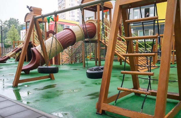 Een binnenplaats van hoogbouw met een moderne en grote speeltuin van hout en plastic op een regenachtige zomerdag zonder mensen. lege buitenspeeltuin. een plek voor kinderspelletjes en sport.