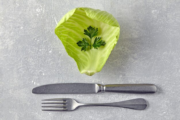 Een blad witte kool en een takje peterselie met tafelsnitten op een grijze betonnen tafel Diet food concept Bovenbeeld met kopieerruimte