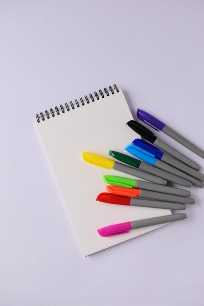 Een blanco notitieblok en gekleurde viltstiften op een witte achtergrond Veelkleurige viltstiften voor