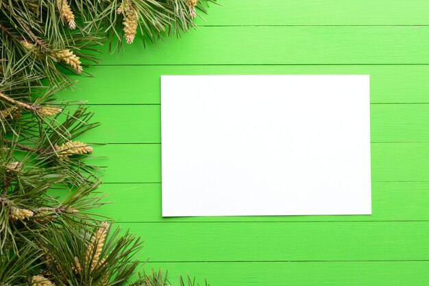 Een blanco vel papier tussen pijnboomtakken op een groene houten achtergrond