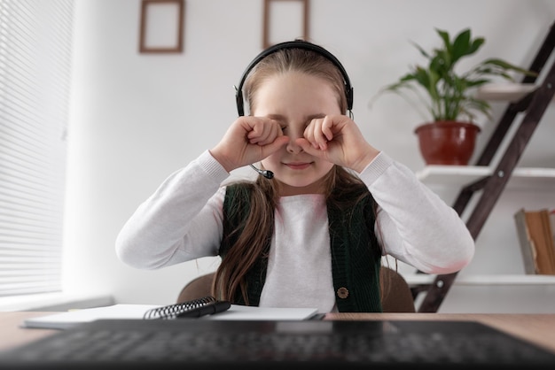 Een blank meisje zit voor een laptop naar een video te kijken en wrijft met haar handen in haar ogen De afhankelijkheid van het kind van internet en gadgets Video-inhoud en zichtproblemen