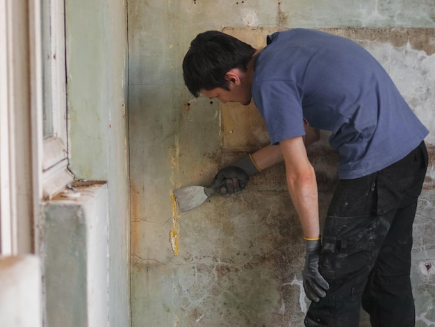 Een blanke brunette man maakt de muur schoon met één gehandschoende hand met behulp van een spatel