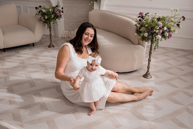 Een blanke brunette moeder zit op de grond in een kamer met een dochtertje in een kamer met een lentedesign