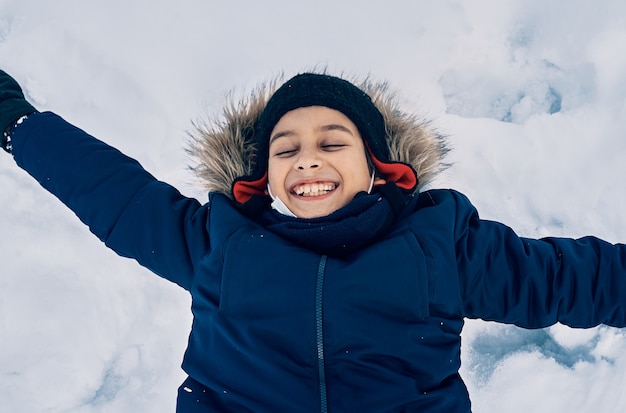 Een blanke jongen die lacht liggend in de sneeuw