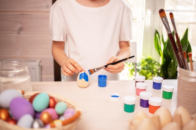 Een blanke jongen in een wit t-shirt schildert eieren om de paasvakantie met felle kleuren te vieren