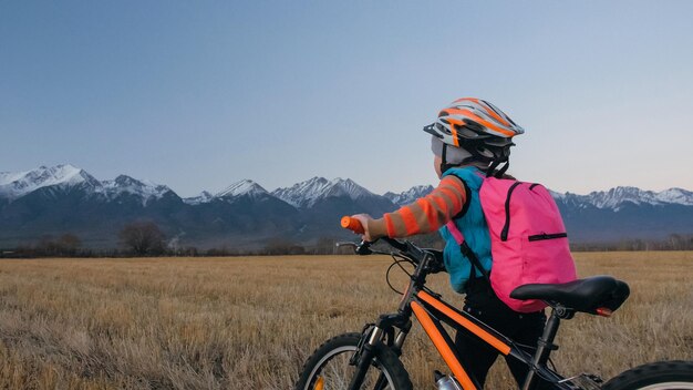 Een blanke kinderen lopen met een fiets in een tarweveld Klein meisje loopt een zwarte oranje cyclus