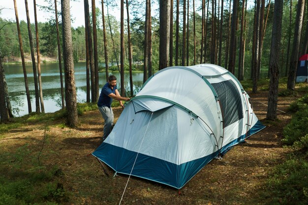 Een blanke man die een tent opzet in een dennenbos.