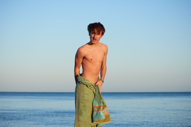 Een blanke man die zichzelf afdroogt met een groene handdoek op een strand met een zee op de achtergrond