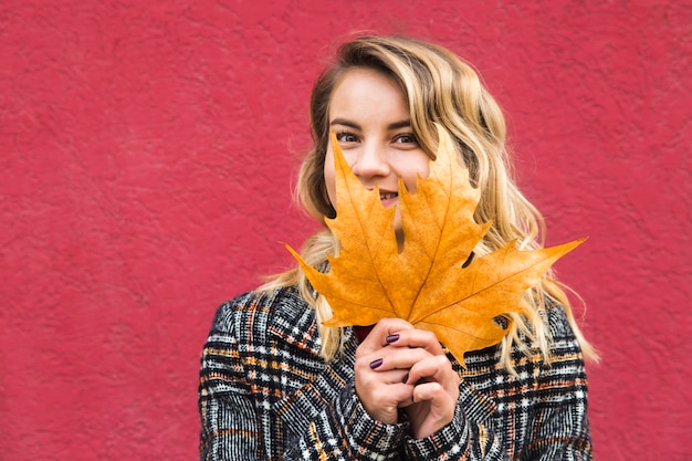 Een blanke vrouw kijkt en bedekt haar gezicht met een herfstblad.