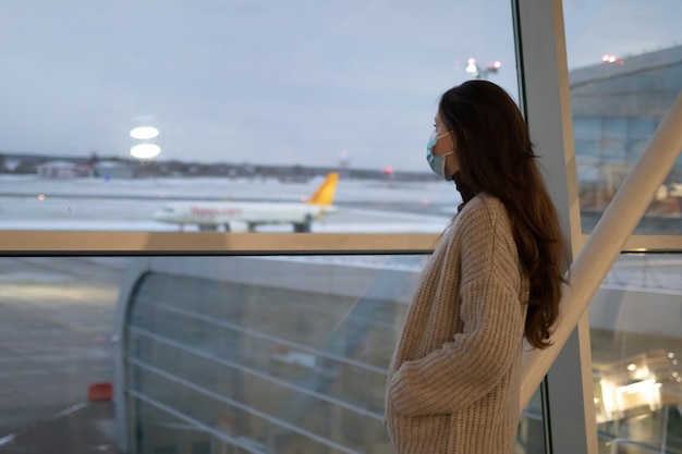 Een blanke vrouw staat bij het raam op de luchthaven en kijkt naar het vliegtuig