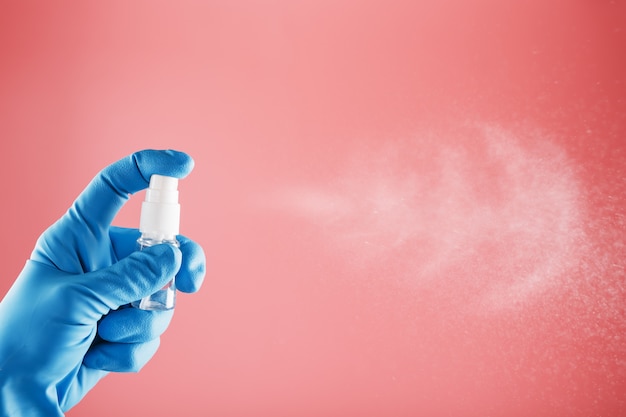 Een blauw gehandschoende hand houdt een ontsmettingsmiddel op een roze achtergrond. Antiseptische behandeling van handen door bacteriën Sanitizer.