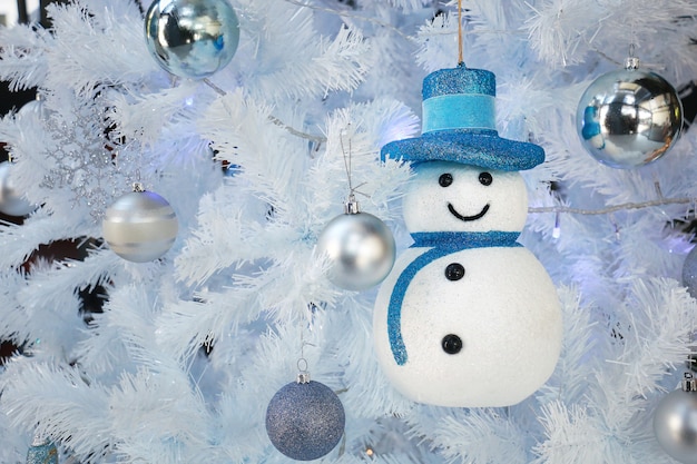 Een blauwe hoedensneeuwman hangt op witte Kerstmisboom voor gevierd groetseizoen