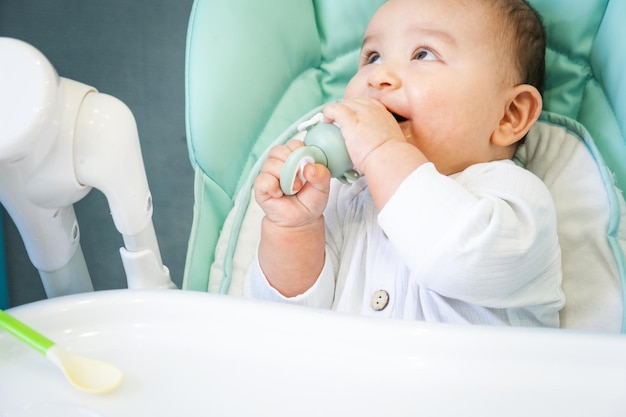 Een blije en tevreden baby eet bananenpuree uit een tepel Introductie van aanvullende voedingsmiddelen gezonde babyvoeding de baby aan tafel voeden