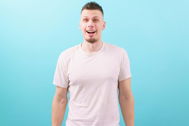 Een blije en verraste man in een wit t-shirt kijkt naar de camera op blauw Studio White Young