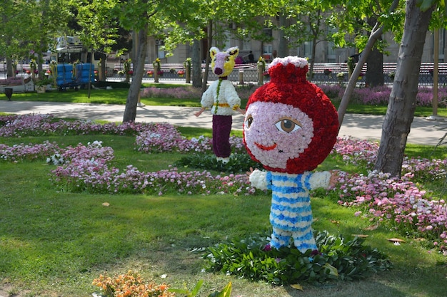 Een bloementuin met een figuur van een meisje met een rode hoed en een blauw gestreept overhemd.