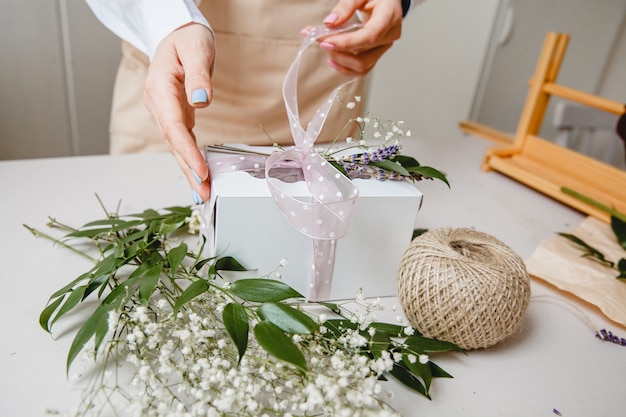 Een bloemist versiert een geschenkdoos met bloemen en een lint op een wit bureaublad