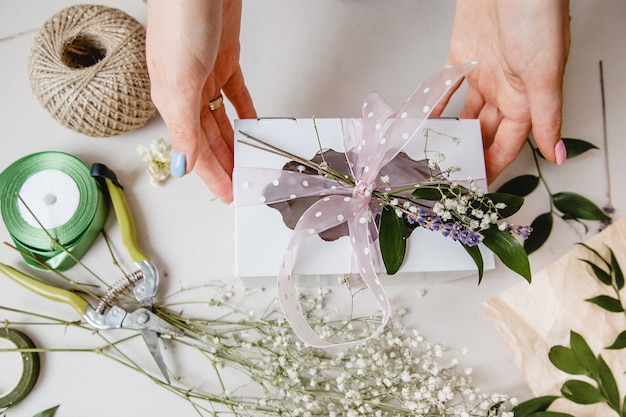 Een bloemist versiert een geschenkdoos met bloemen en een lint