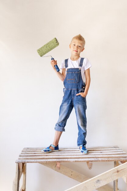 Een blond kind staat op een bouwladder en een roller in zijn handen