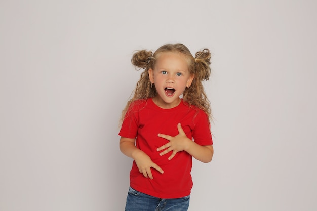 een blond meisje in een rood T-shirt en een spijkerbroek met paardenstaarten toont emoties