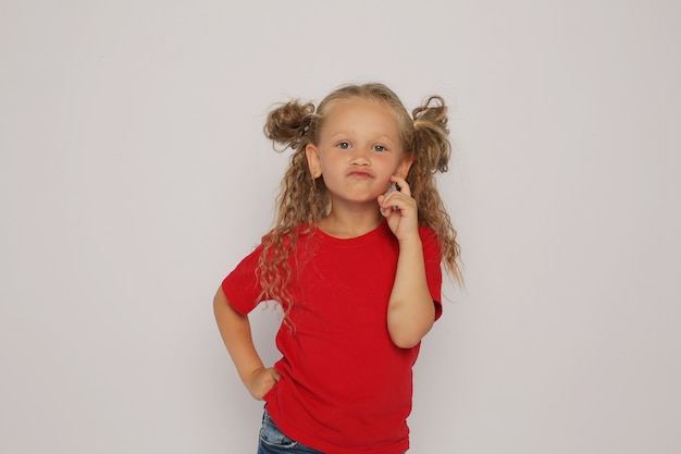 een blond meisje in een rood T-shirt en een spijkerbroek met paardenstaarten toont emoties