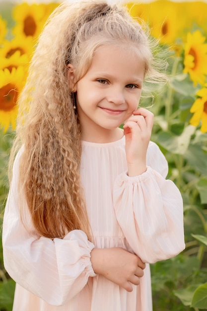 een blond meisje met lang haar in een linnen jurk staat in een bloeiend veld met zonnebloemen