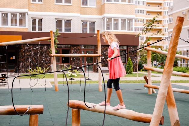 Een blond schoolmeisje speelt op de speelplaats in de achtertuin van de stad.