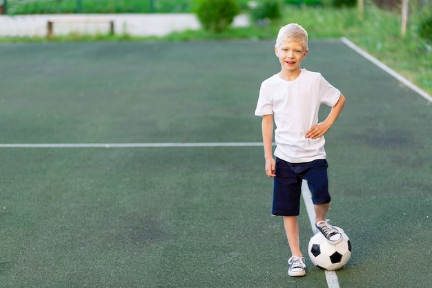 een blonde jongen in een sportuniform staat op een voetbalveld met een voetbal