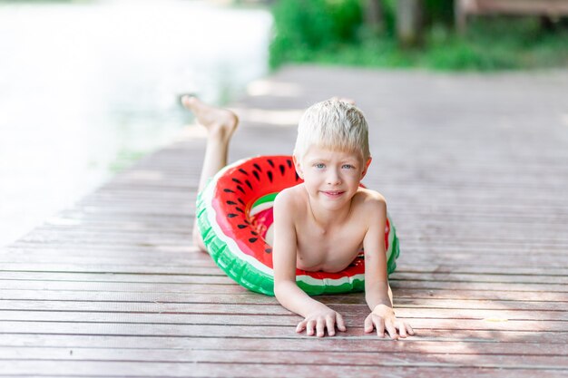 een blonde jongen ligt op een pier bij het water met een rode en groene vlotter