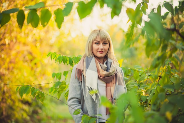 Een blonde vrouw met een kort kapsel loopt door het bos in een grijze wollen jas en een geruite sjaal