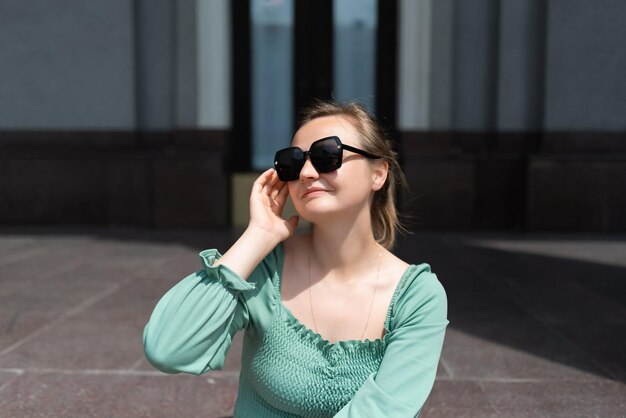 Een blonde vrouw met een zonnebril en een groene blouse op straat in de zomer