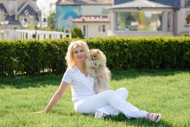 Een blonde vrouw zit op het gras met een Yorkshire terriër in haar armen