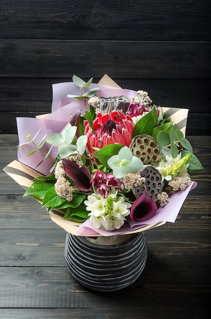 Een boeket bloemen op een donkere houten achtergrond. Boeket met protea, orchidee, papaver, sappig ..