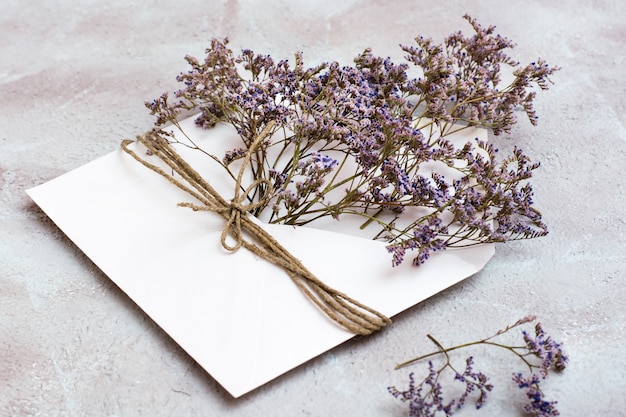 Een boeket gedroogde bloemen in een lichte envelop vastgebonden met een touw op een gestructureerde achtergrond. Groet romantische kaart