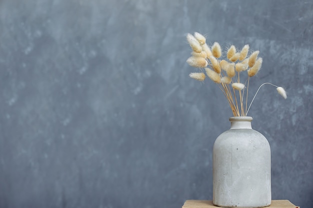 Een boeket gedroogde bloemen in een witte keramische vaas, op een grijsblauwe achtergrond.