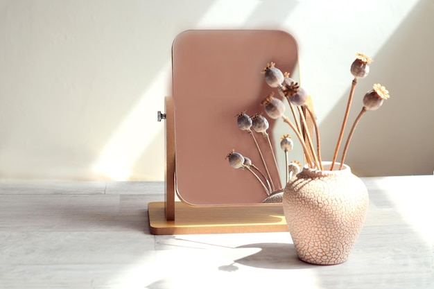 Een boeket gedroogde papaverbloeiwijzen wordt weerspiegeld in een spiegel die op een grijze tafel staat, de stralen van de zonschaduw zijaanzicht