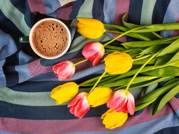 Een boeket gele en roze tulpen met een kop koffie op een kleurrijke gestreepte vrouwelijke trui