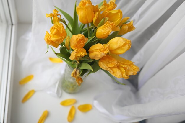 Een boeket gele tulpen in een vaas op de vensterbank. Een cadeau voor een vrouwendag van gele tulpenbloemen. Mooie gele bloemen in een vaas bij het raam.