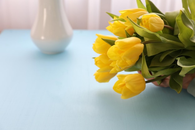 Een boeket gele tulpen op een blauwe achtergrond naast een vaas