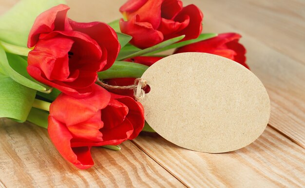 Een boeket rode tulpen en een blanco briefje op een houten tafel