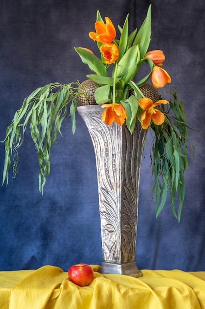 Een boeket rode tulpen in een hoge Art Deco vaas op een tafel met een geel tafelkleed.