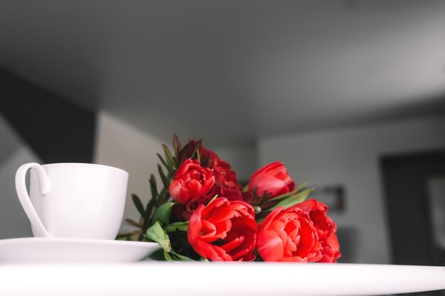 Een boeket rode tulpen op tafel en een witte kop koffie. Concept van romantiek