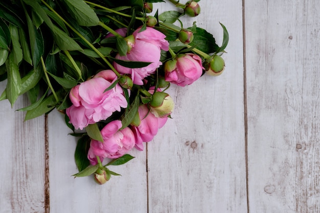 Een boeket roze karmozijnrode pioenrozen ligt close-up op een houten tafel