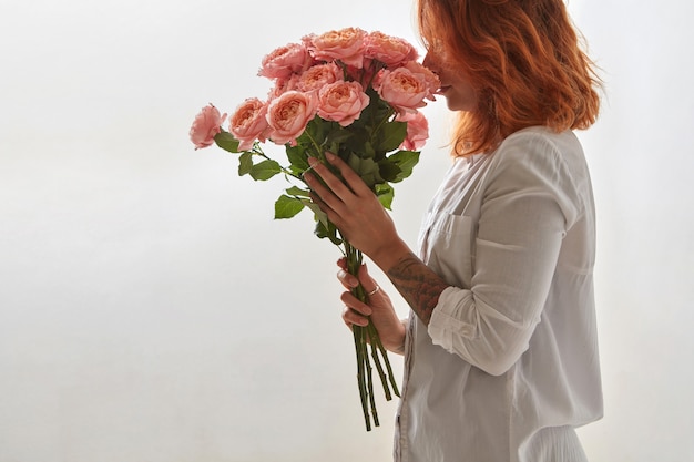 Een boeket roze rozen wordt in handen gehouden door een roodharig jong meisje op een grijze achtergrond met kopieerruimte. Valentijnsdag