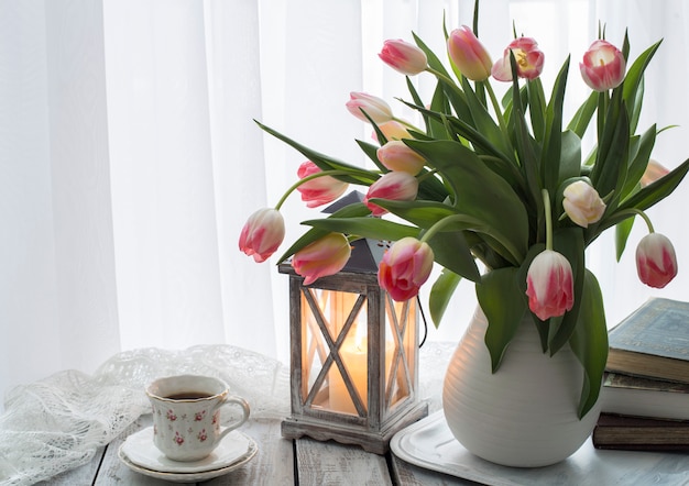 een boeket roze tulpen in een vaas, boeken, een kaars en een kopje koffie