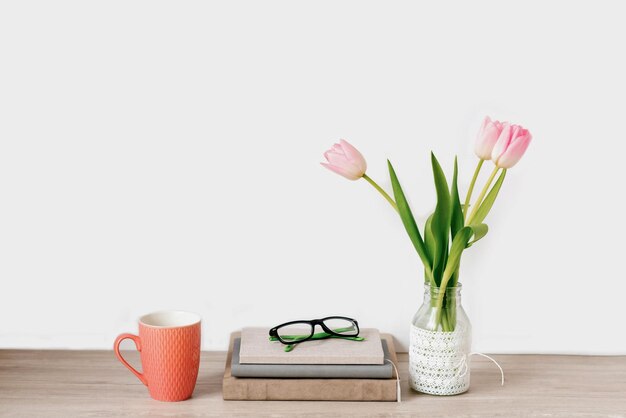 Een boeket roze tulpen van lentebloemen in een vaas staat op het bureaublad naast notitieboekjes