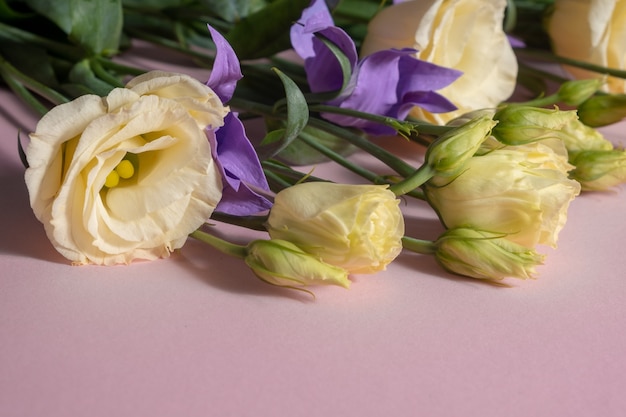 Een boeket van lichtgele eustoma en lila clematis op een roze ondergrond.