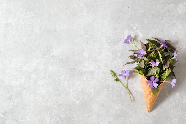 Foto een boeket van lila bloemen in een wafelkegel op een grijze tafel. lente concept.