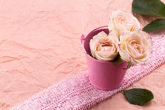 Een boeket van mooie rozen bevindt zich in een kleine emmer op een kantlint op een roze ambachtachtergrond